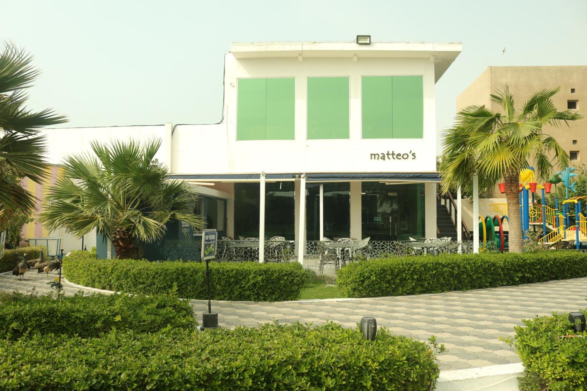 מנאמה Lagoona Beach Luxury Resort And Spa מראה חיצוני תמונה The photo shows a building with the name "matteo's" displayed prominently on the front. The structure features large windows and green shutters. There is a landscaped area in front with bushes and palm trees, along with a paved pathway leading up to 