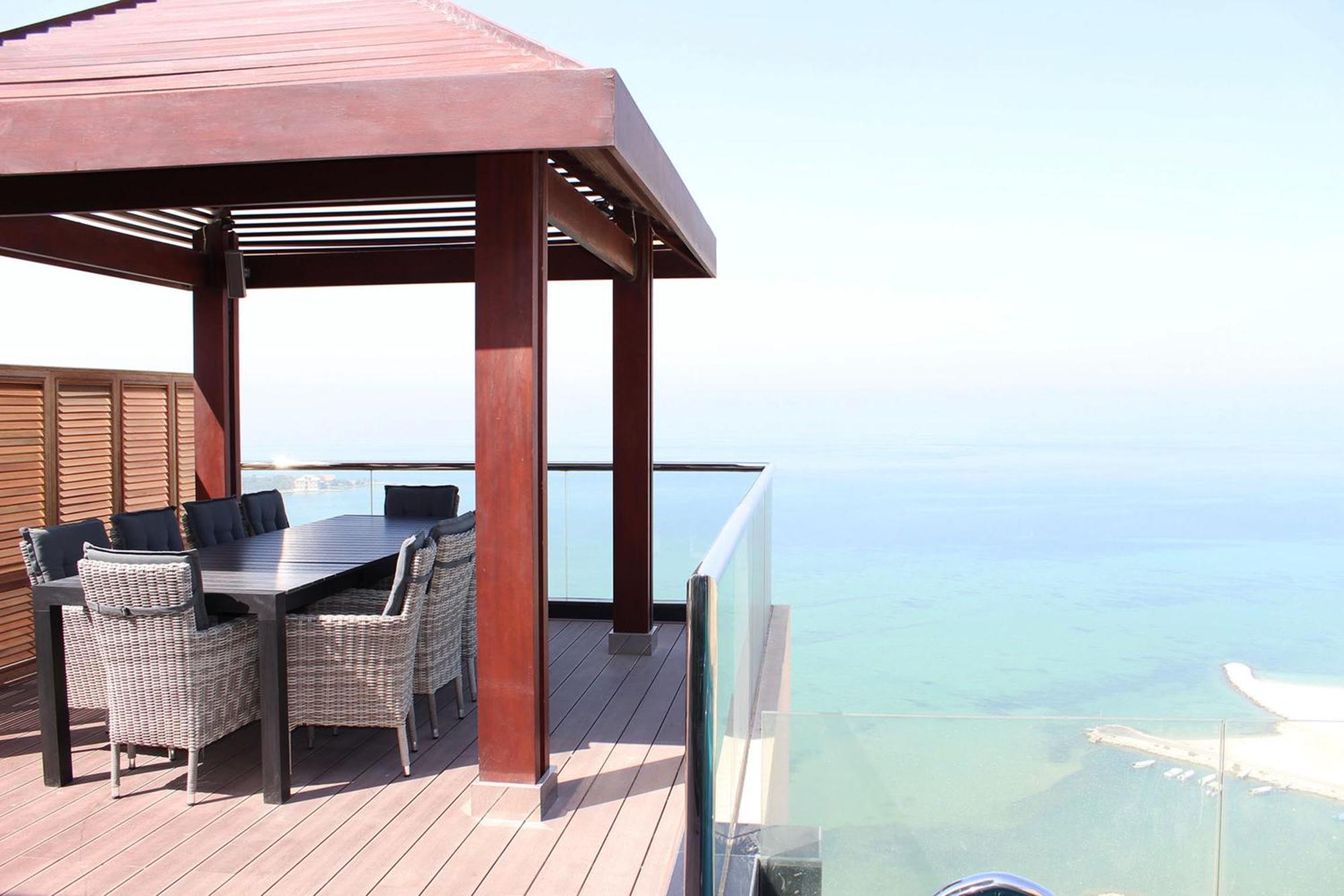 מנאמה Lagoona Beach Luxury Resort And Spa מראה חיצוני תמונה The photo showcases a stylish outdoor patio or terrace area. It features a wooden structure with a sloped roof, providing a shaded space. There is a large table made of dark wood, surrounded by several wicker chairs. The patio is elevated and has gla
