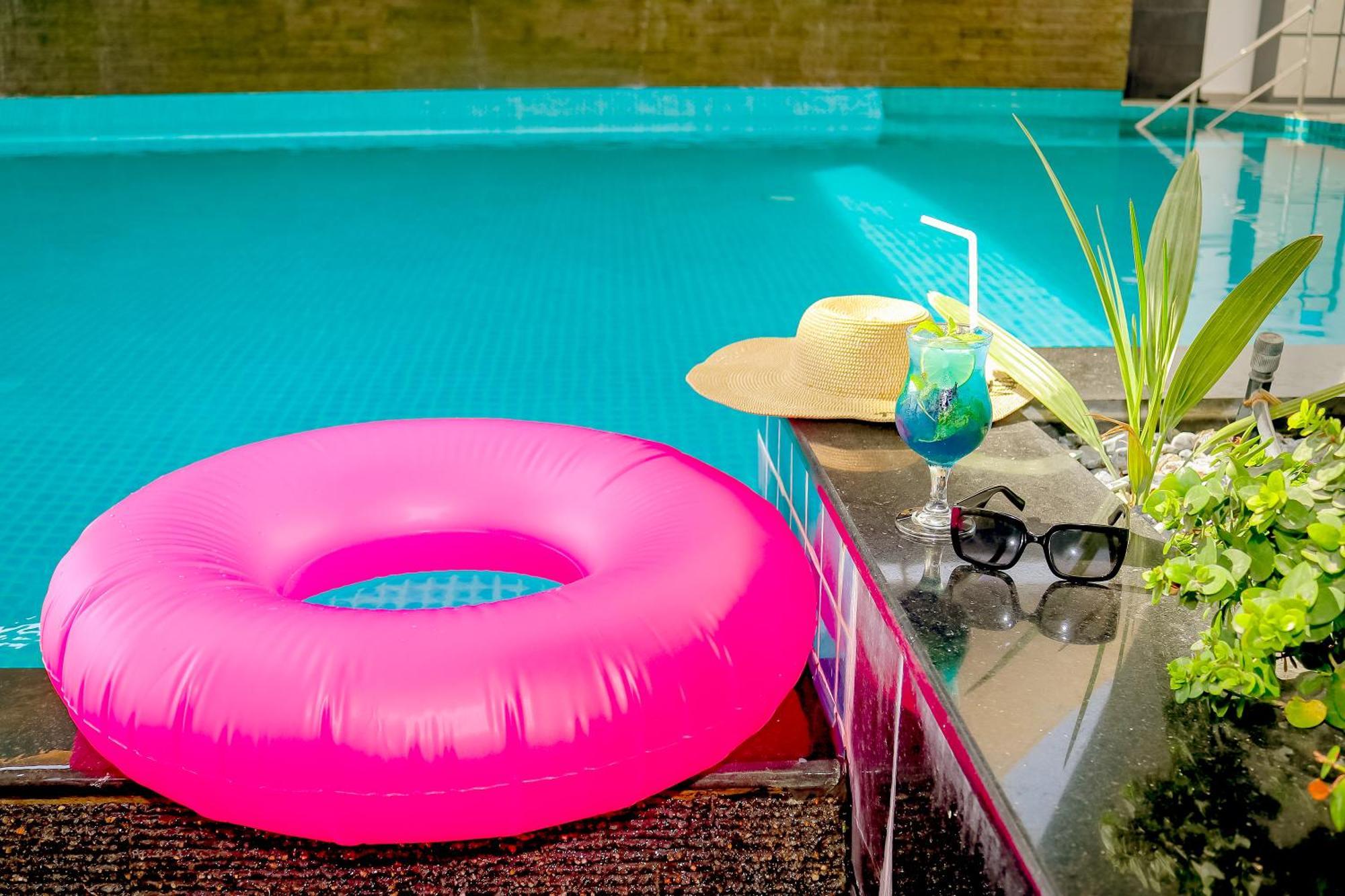 מנאמה Lagoona Beach Luxury Resort And Spa מראה חיצוני תמונה The photo shows a vibrant and inviting scene by a swimming pool. In the foreground, there is a large pink inflatable float and a stylish straw hat. Next to the float, a refreshing cocktail in a glass is displayed, complete with a straw and garnishes.