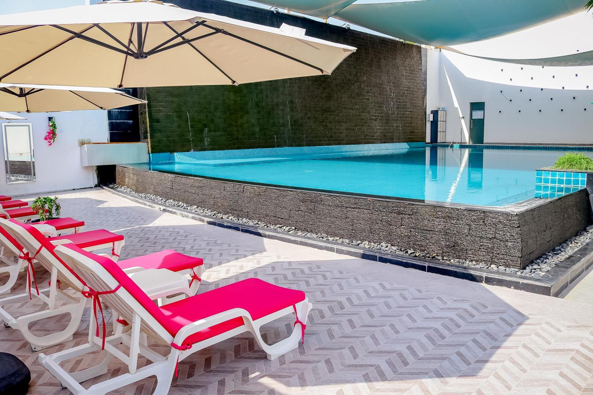 מנאמה Lagoona Beach Luxury Resort And Spa מראה חיצוני תמונה The photo shows a pool area featuring a rectangular swimming pool with clear blue water. Surrounding the pool are light-colored lounge chairs with pink cushions, positioned under large umbrellas for shade. The pool is bordered by a textured wall, and