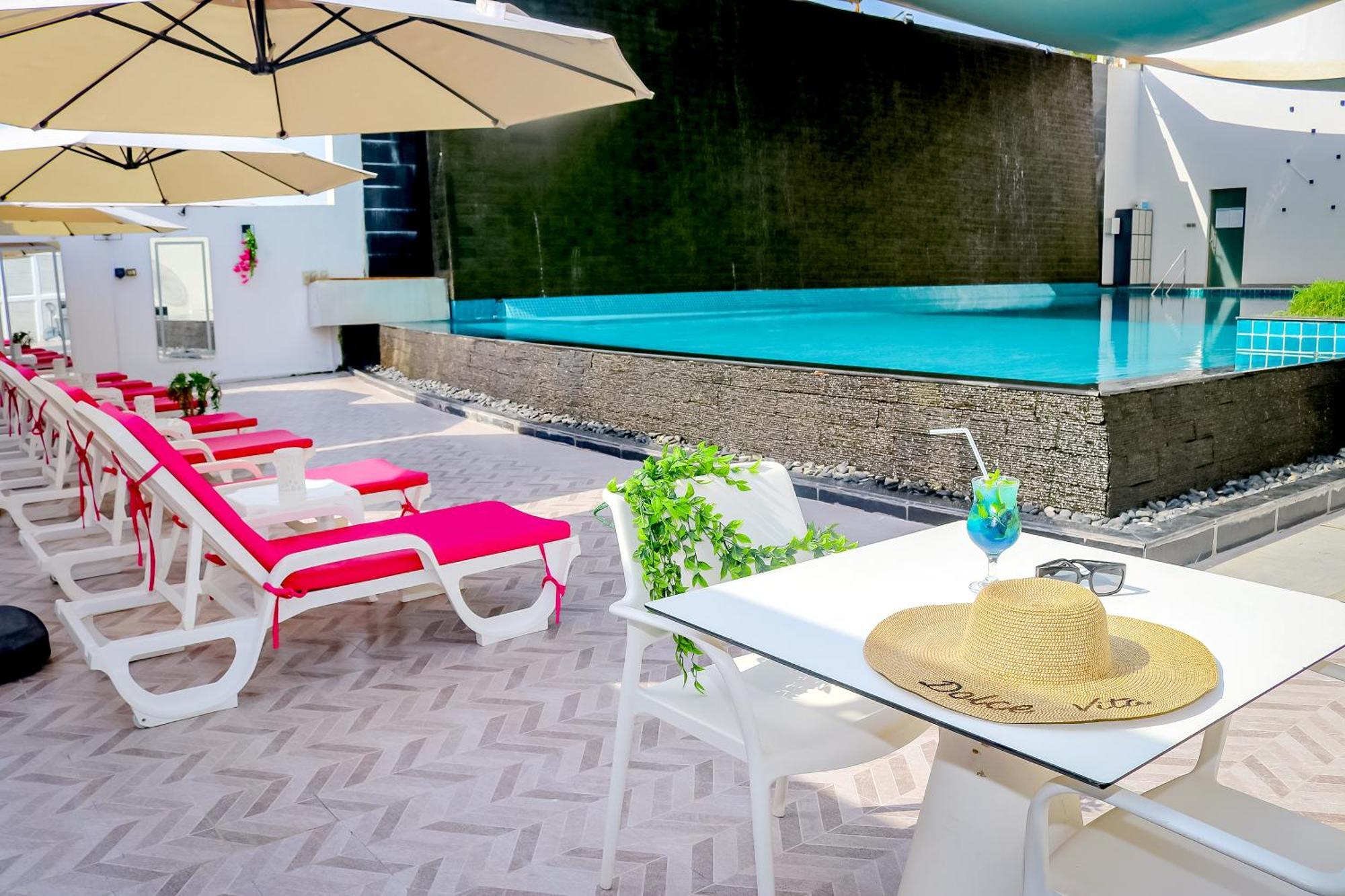 מנאמה Lagoona Beach Luxury Resort And Spa מראה חיצוני תמונה The photo shows a sunny poolside area with bright red lounge chairs arranged neatly beside a swimming pool. There are large beige umbrellas providing shade. A small table is set up with a straw hat and a colorful drink, suggesting a relaxed, tropical