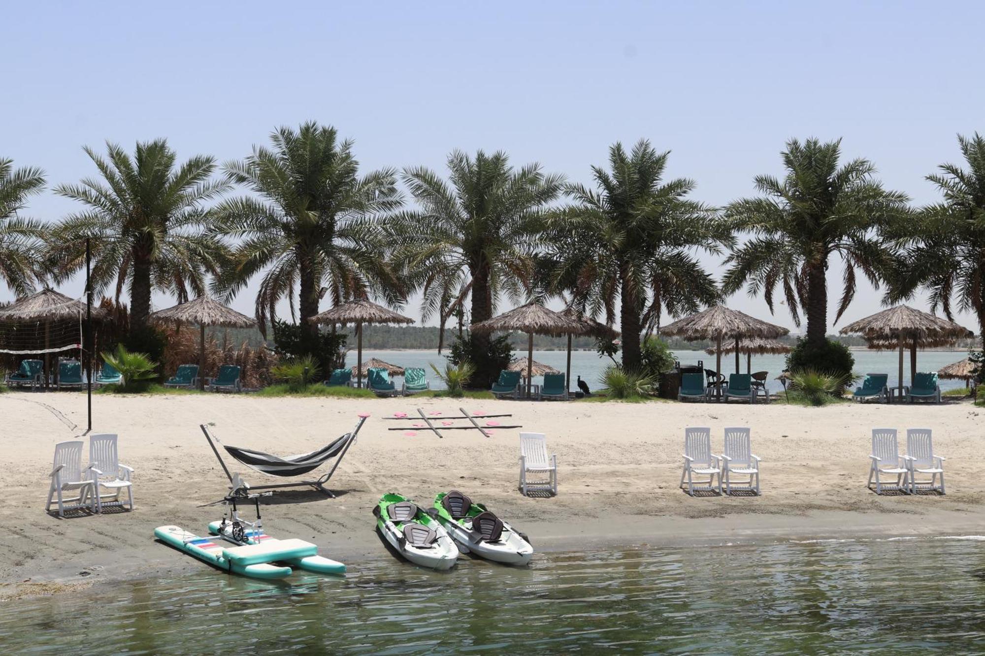 מנאמה Lagoona Beach Luxury Resort And Spa מראה חיצוני תמונה The photo depicts a serene beach scene with several palm trees lining the shore. There are thatched umbrellas providing shade, and a few lounge chairs are positioned on the sand. A hammock is set up between two supports, inviting relaxation. In the f