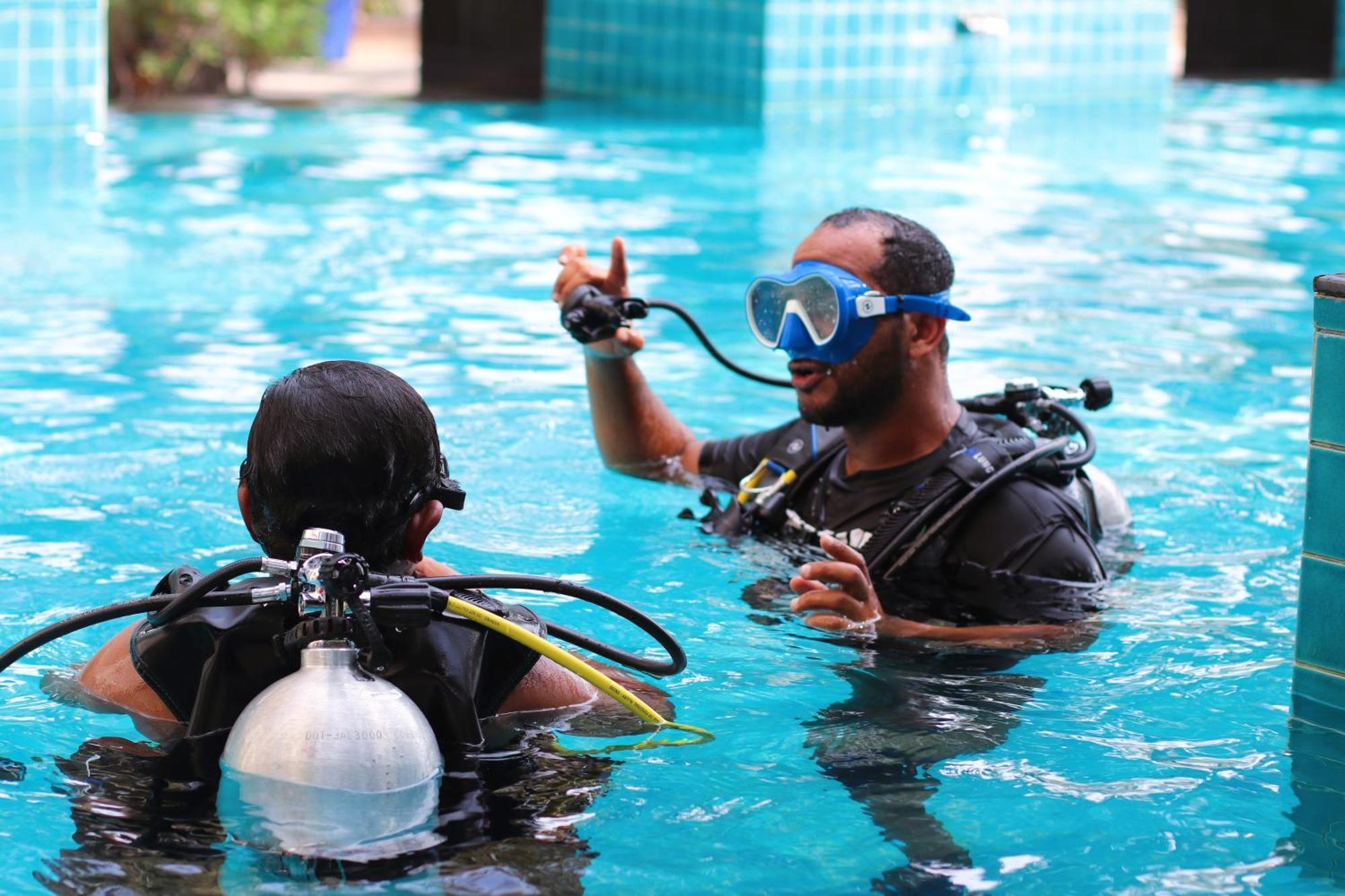 מנאמה Lagoona Beach Luxury Resort And Spa מראה חיצוני תמונה The photo shows two divers in a pool. One diver is wearing a scuba mask and is speaking to the other diver, who is also equipped with scuba gear. They appear to be engaged in a discussion, possibly related to diving instructions or safety. The water 