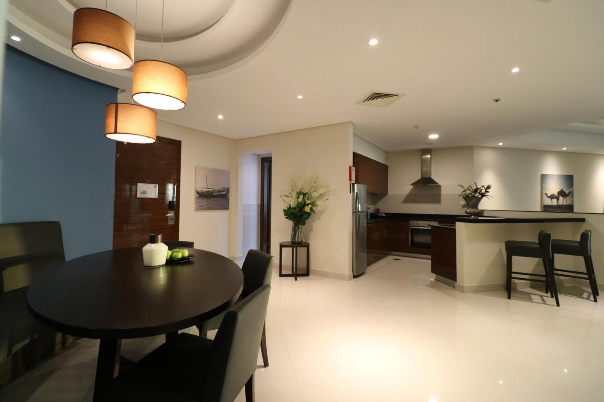 מנאמה Lagoona Beach Luxury Resort And Spa מראה חיצוני תמונה The photo shows a modern, open-concept dining and kitchen area. On the left, there is a round dining table with black chairs, accompanied by a few decorative elements like a small vase and some fruit. The walls have a combination of light and dark to