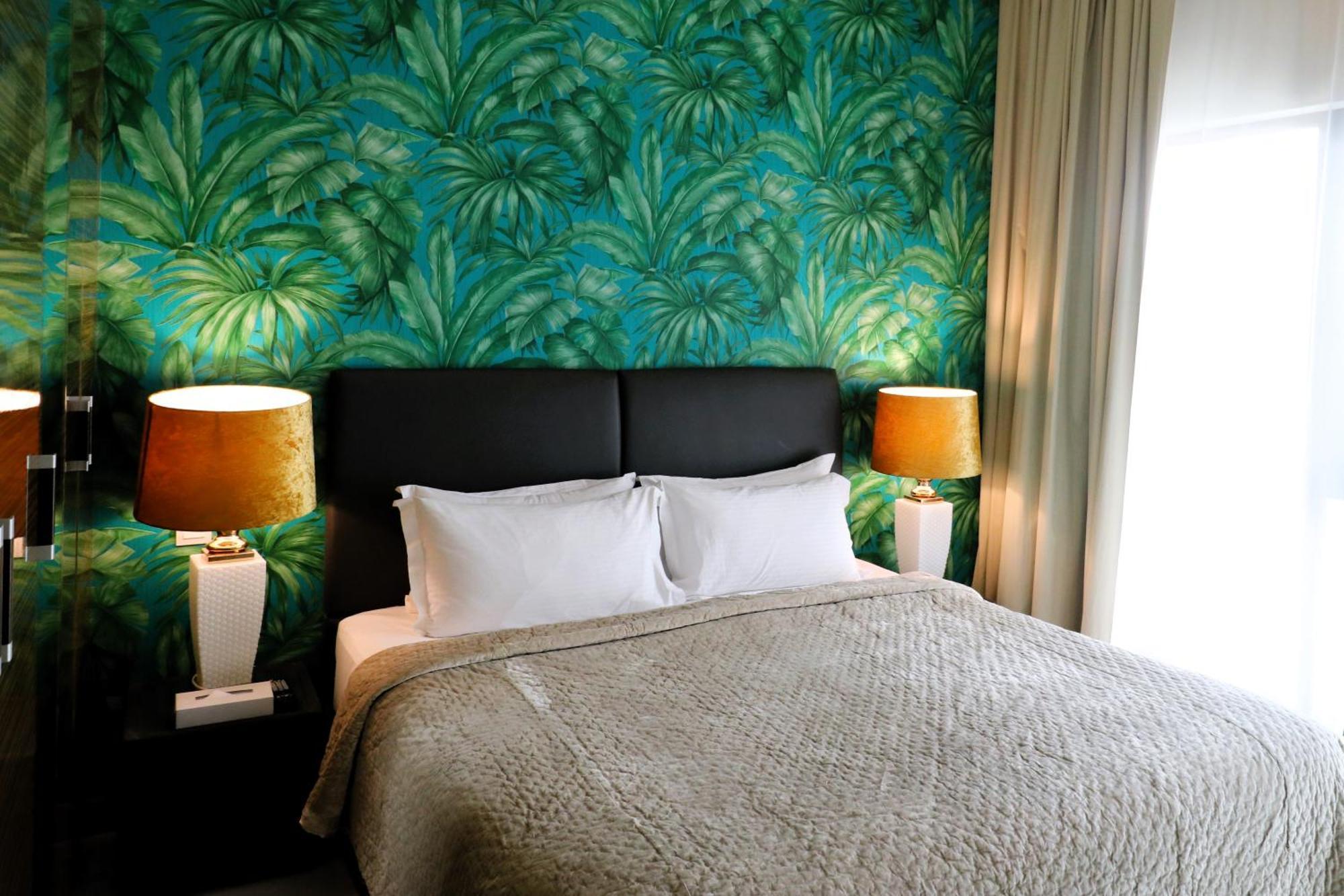 מנאמה Lagoona Beach Luxury Resort And Spa מראה חיצוני תמונה The photo shows a stylish bedroom featuring a large bed with white pillows and a gray blanket. The headboard is upholstered in black, providing a modern touch. Behind the bed, there is a vibrant green wallpaper with a tropical leaf pattern, adding a 