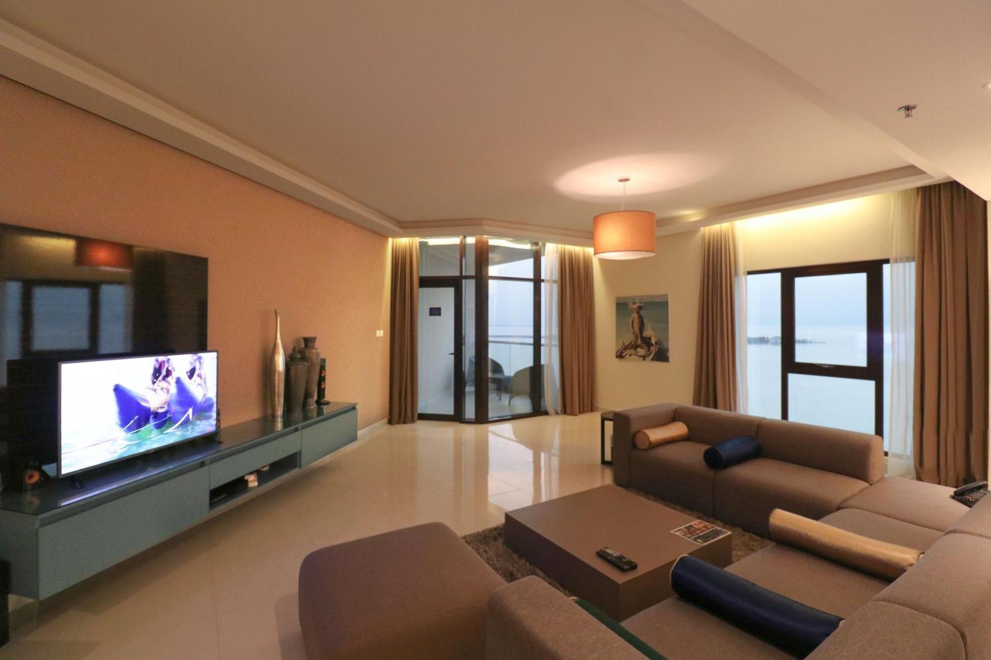 מנאמה Lagoona Beach Luxury Resort And Spa מראה חיצוני תמונה The photo shows a modern living room with a sleek design. There is a large wall-mounted television on a contemporary entertainment unit, with decorative items placed beside it. The room features a comfortable sectional sofa in light tones, with a cof
