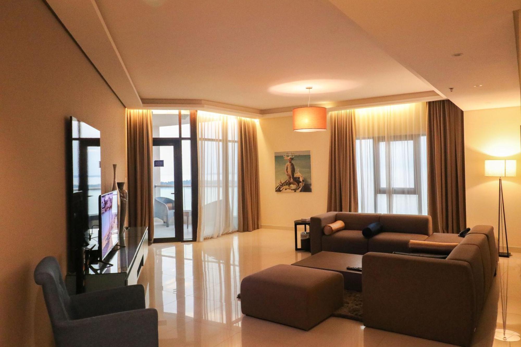 מנאמה Lagoona Beach Luxury Resort And Spa מראה חיצוני תמונה The photo shows a modern living room with a spacious and elegant design. It features a large couch in neutral tones, a soft ottoman, and a stylish coffee table. The walls are painted in a light color, and there are large windows with sheer curtains a