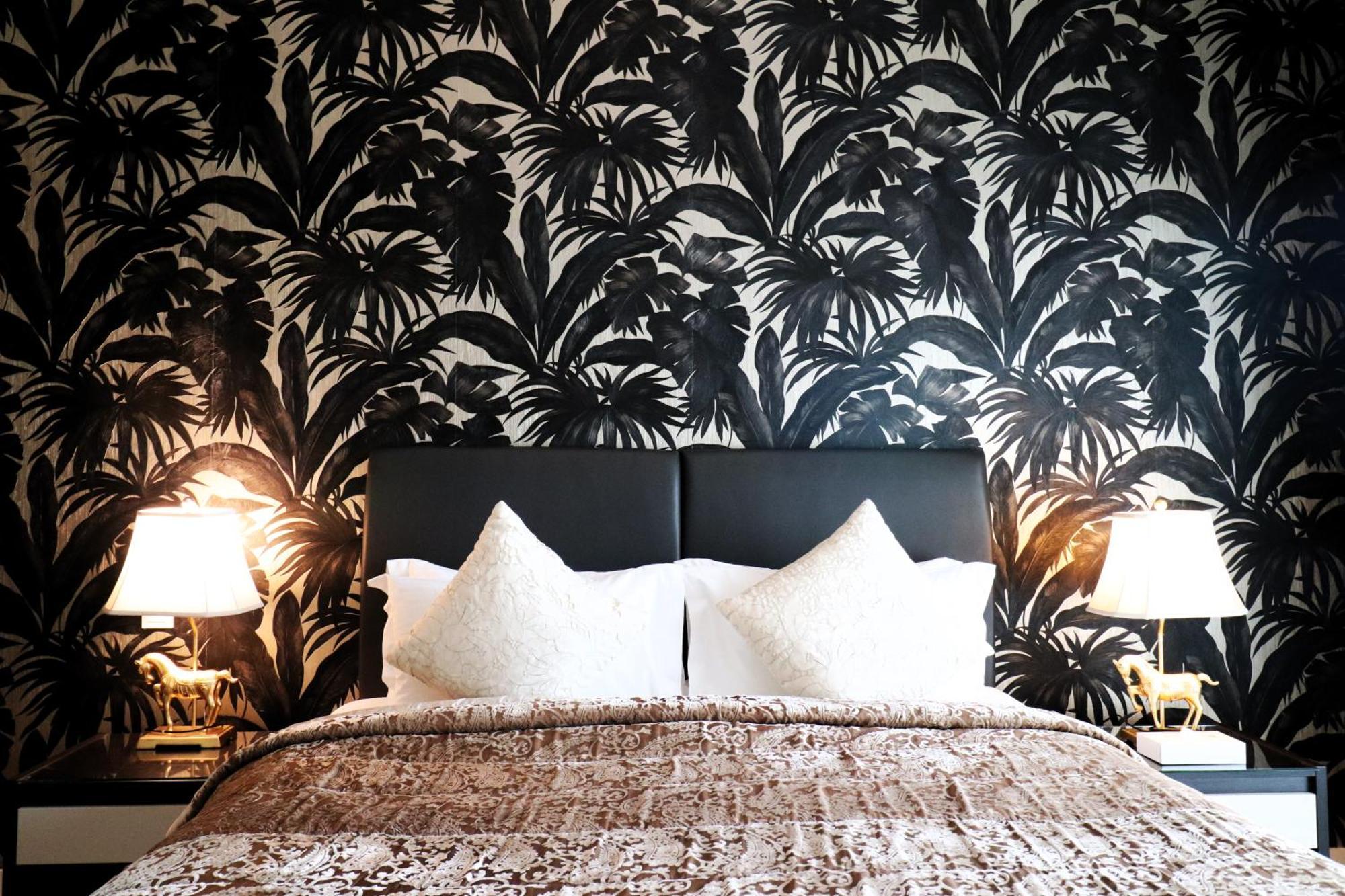 מנאמה Lagoona Beach Luxury Resort And Spa מראה חיצוני תמונה The photo depicts a stylish bedroom featuring a distinctive wall covered in a black and white tropical foliage wallpaper. The bed has a modern black headboard and is adorned with white pillows, creating a clean and elegant look. A textured brown thro