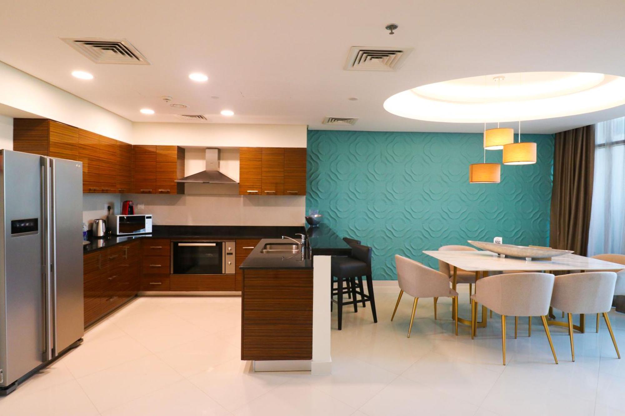 מנאמה Lagoona Beach Luxury Resort And Spa מראה חיצוני תמונה The photo shows a modern kitchen and dining area. The kitchen features wooden cabinets, sleek appliances including a stainless steel refrigerator, microwave, and an oven. There is a dark countertop and a small breakfast bar with high stools. The wall